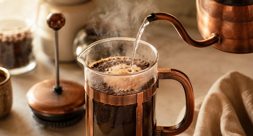 Eau chaude versée dans une cafetière à piston en verre, croûte de café qui gonfle à la surface